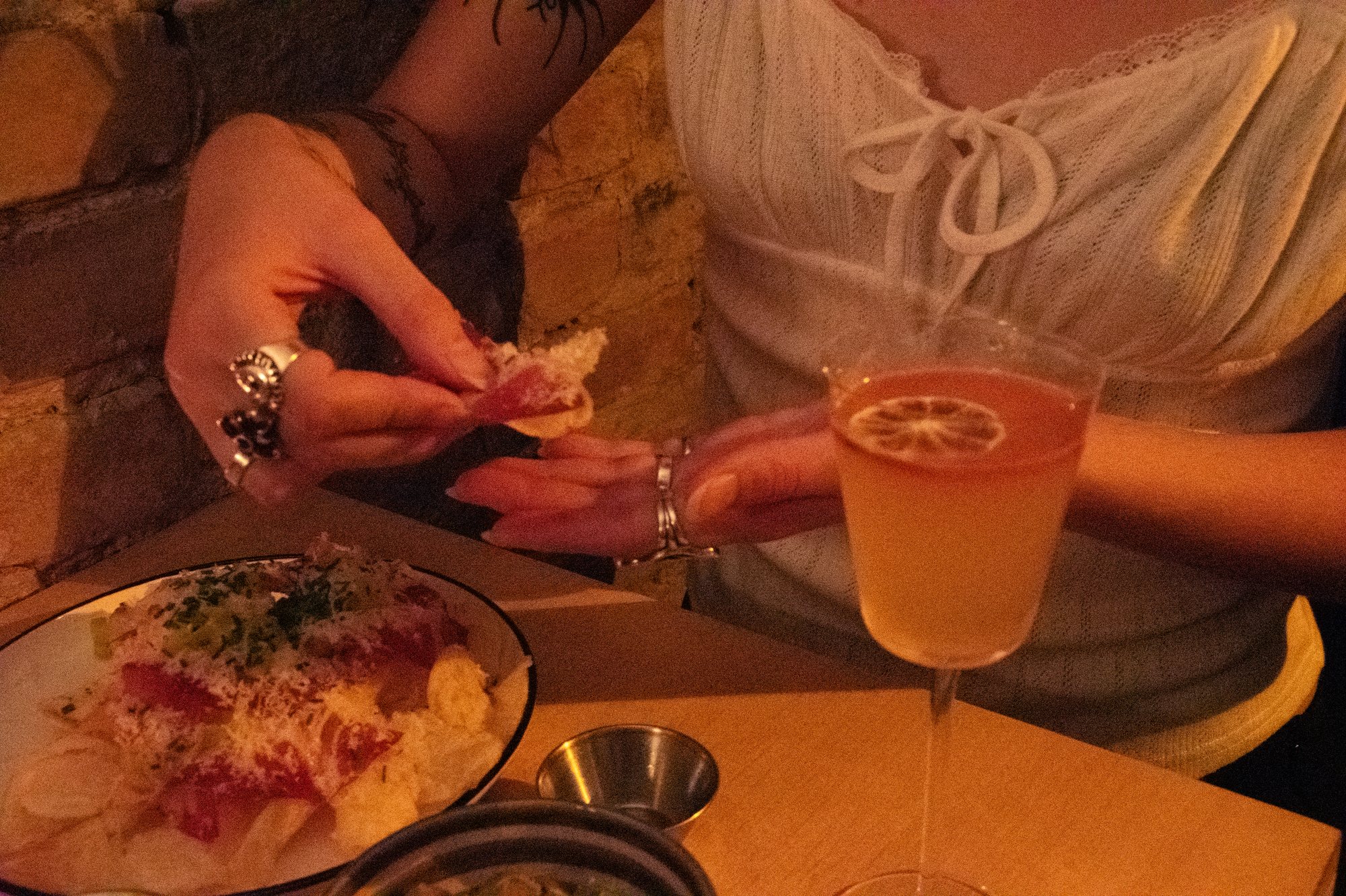 A guest reaching for a bite of loaded chips beside a citrus cocktail on a bar table