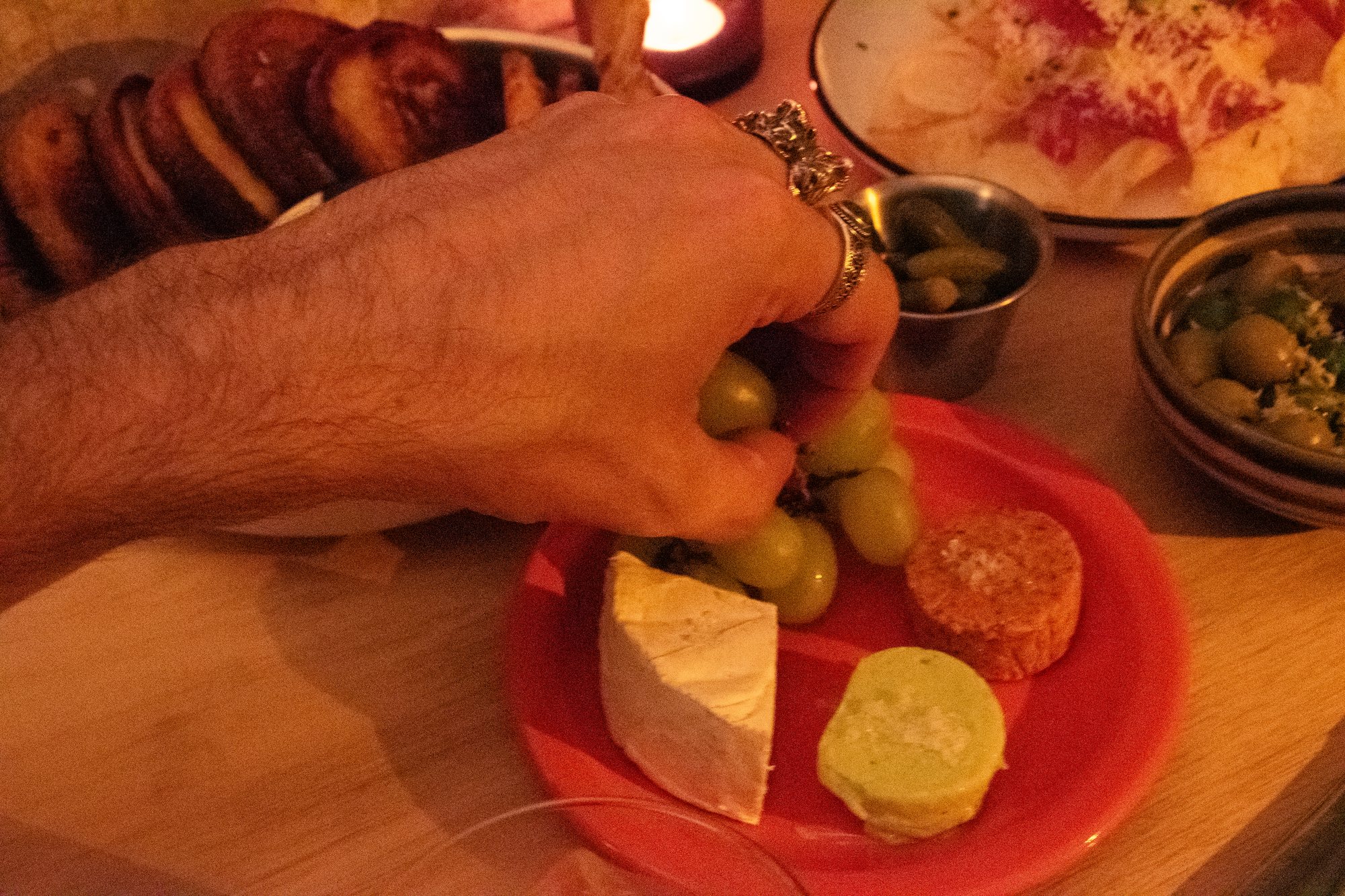 A hand reaching for grapes on a plate of brie, whipped feta, and crostini